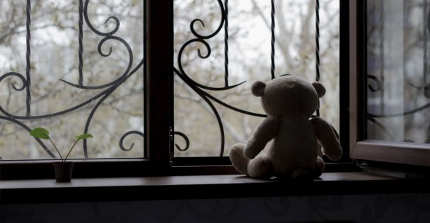 Ein einsamer Teddybär vor einem vergitterten Fenster.