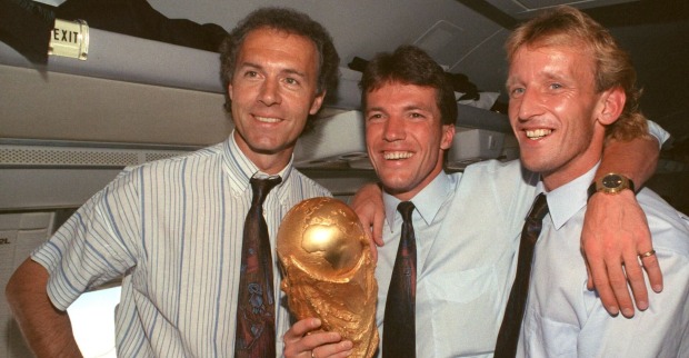Andreas Brehme hält mit Lothar Matthäus und Franz Beckenbauer den WM-Pokal