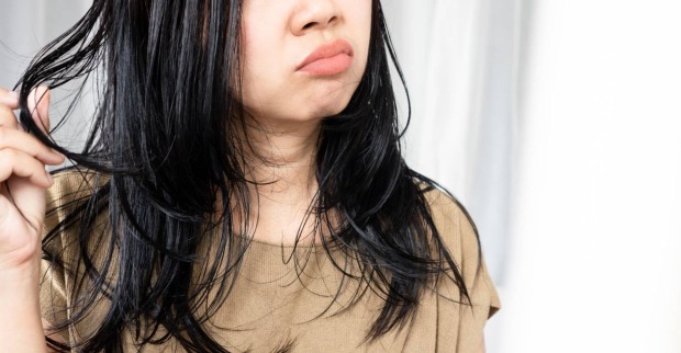 Frau mit fettigen Haaren mit einem unglücklichen Gesichtsausdruck, die in den Spiegel blickt