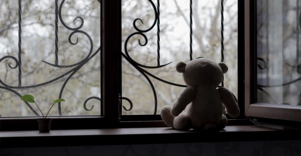 Ein einsamer Teddybär sitzt vor einem vergitterten Fenster.