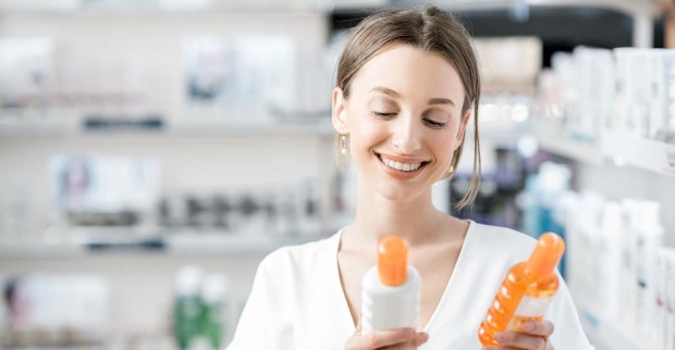 Frau mit Sonnencreme-Flaschen in der Hand | Credit: iStock.com/RossHelen