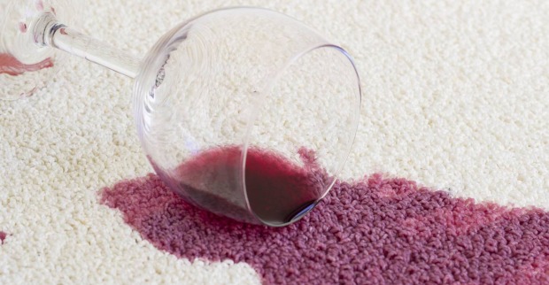 Verschüttetes Glas mit Rotwein auf weißen Teppich