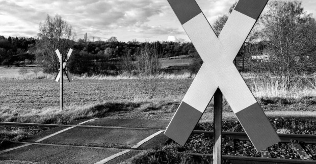 Ein düsteres Schwarz-weiß-Bild von einem Bahnübergang mit Andreaskreuz.