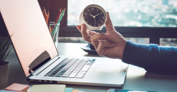 Schreibtisch mit Laptop, Uhr und Stifteköcher