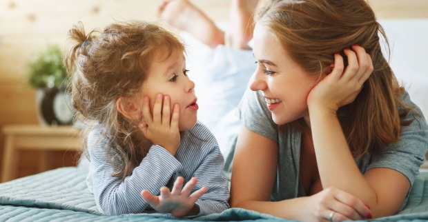 Kleinkind und ältere Schwester liegen gemeinsam auf dem Bett, dabei haben sie die Hände an den Kopf gestützt