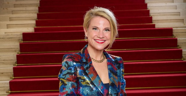 Kristina Sprenger vor einem Treppenaufgang mit einem bunten Anzug.