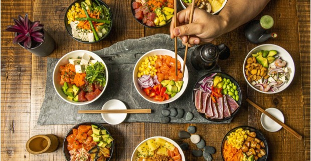 Vogelperspektive auf einen Tisch mit 7 verschiedenen Sushi Bowls.