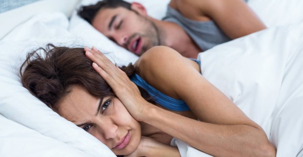 Junge Frau, die wach neben ihrem Partner im Bett liegt und sich die Ohren zuhält