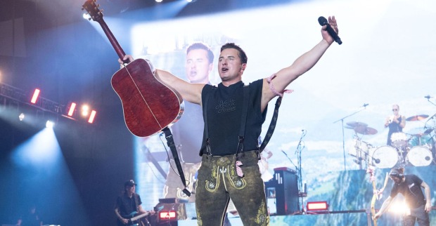 Andreas Gabalier auf der Bühne mit einer Lederhose und einer Gitarre.