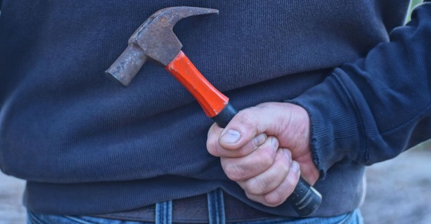 Ein Mann hält einen Hammer versteckt hinter seinem Rücken.