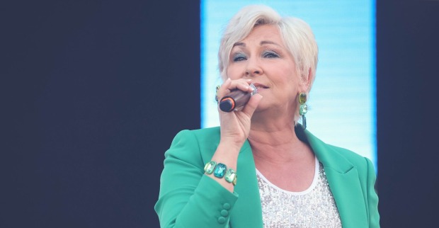 Claudia Jung mit einem türkisen Blazer, einem Mikrofon und kurzen blonden Haaren auf der Bühne.