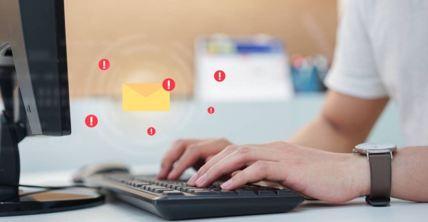 Ein Symbolbild für einen Phishing-Versuch. Illustriertes Briefsymbol über der Tastatur einer Person, die gerade etwas am PC bearbeitet.