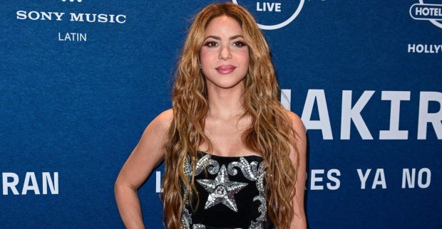 Shakira mit langen, offenen Haaren vor einer blauen Fotowand.