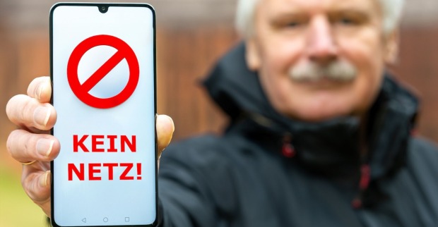 Eine Mann hält eine Handy mit einer "Kein Netz"-Aufschrift in die Kamera.