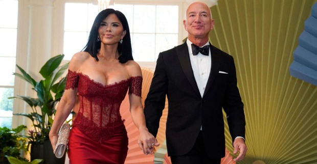 Eine Frau in einem tief ausgeschnittenen roten Kleid hält Händchen mit einem Mann in einem Smoking