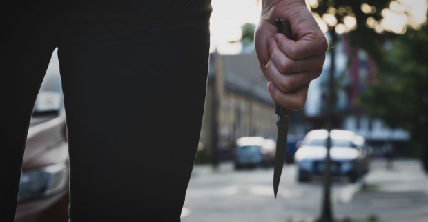 Ein Mann steht in einer Straße und hält ein Messer in der Hand.