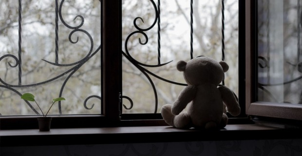 Ein einsamer Teddybär sitzt an einem vergitterten Fenster