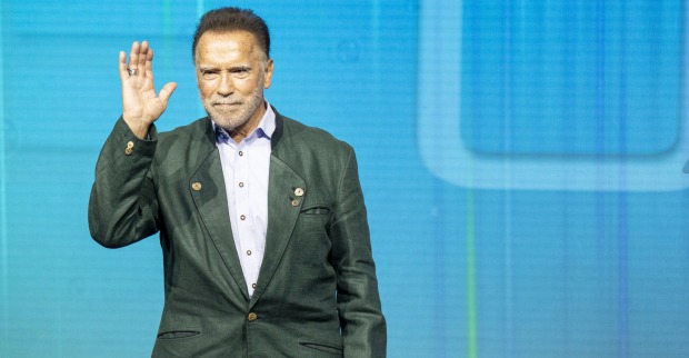 Arnold Schwarzenegger winkt in einem grünen Sakko von der Bühne.