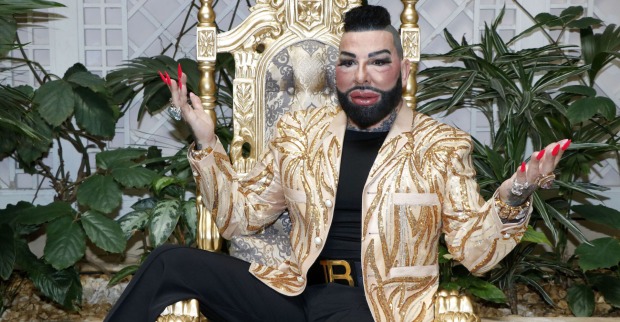 Harald Glööckler mit einer goldenen Jacke auf einem goldenen Stuhl.