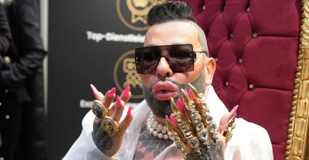Harald Glöckler mit beschmückten Händen und pinken langen Fingernägeln. Er trägt kurze Haare und eine Sonnenbrille.