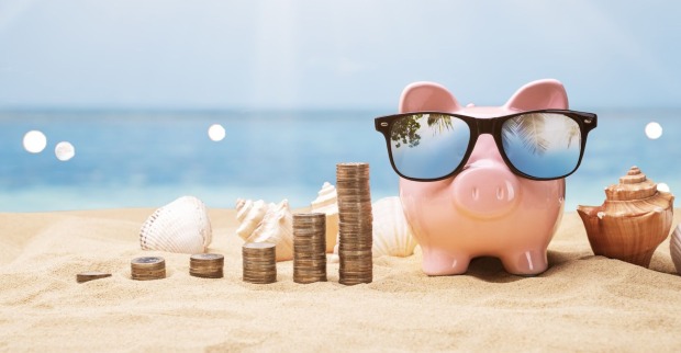 Ein Sparschwein am Strand, daneben Münzstapel
