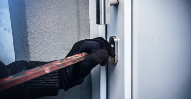 Einbrecher mit schwarzen Handschuhen bricht Tür auf