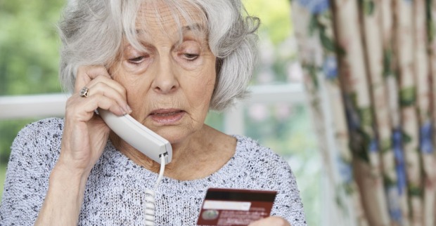 ältere Dame telefoniert und wirft dabei einen Blick auf ihre Kreditkarte