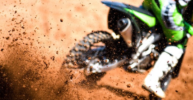 Motocross-Fahrer wirbelt mit den Reifen Schmutz auf