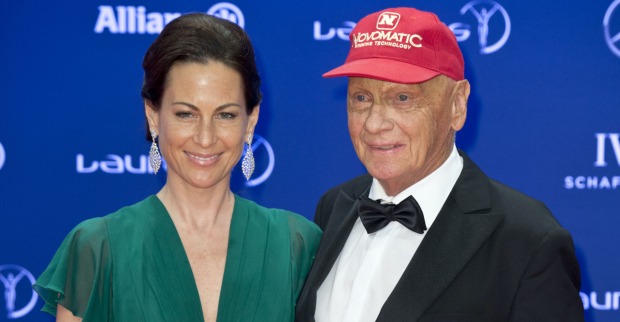 Niki und Birgit Lauda auf einem Event vor einer blauen Fotowand. Sie trägt ein grünes Kleid und Niki Lauda einen Smoking und eine rote Kappe.