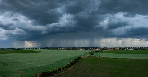 Gewitter mit Starkregen über einem grünen Feld.