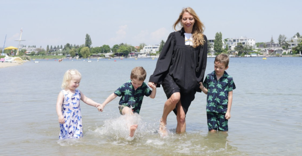 Pfarrerin steht im Talar und drei Kindern im Wasser