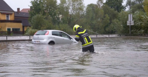 Ein Feuerwehrmann kämpft sich auf einer überflutenden Straße zu einem Auto durch.
