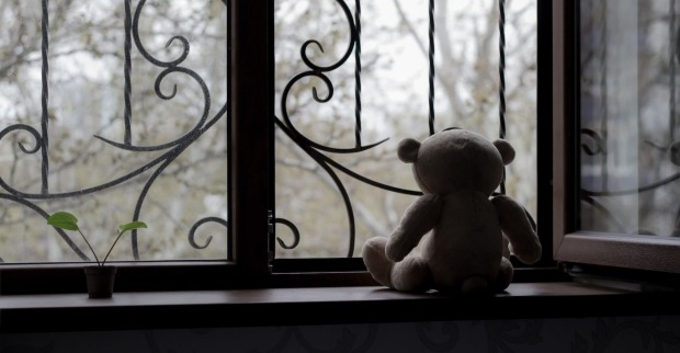 Ein Teddybär sitzt an einem einsamen, vergitterten Fenster.