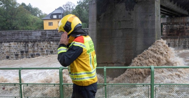 Ein Feuerwehrmann telefoniert, hinter ihm der reißende Wienfluss