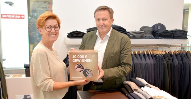 Heidi Mark überreicht Ambros Mayer (Ambros fine clothing) seine Gewinnbox. Er zählt zu den über 65 Unternehmen, die Gewinnchancen bieten.