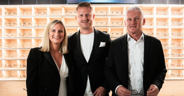 Zwei Männer und eine Frau stehen vor einem Brillenregal
