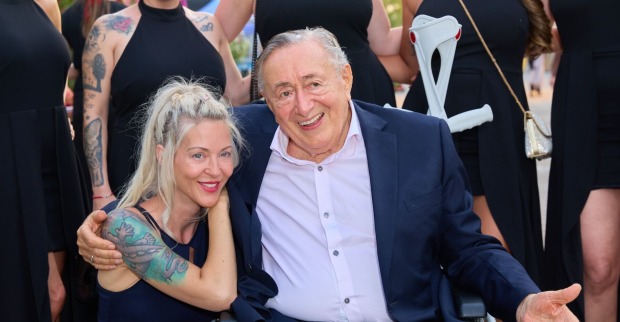 Simone kniet neben dem im Rollstuhl sitzenden Richard Lugner, er hat den Arm um sie gelegt. Beide lachen entspannt.