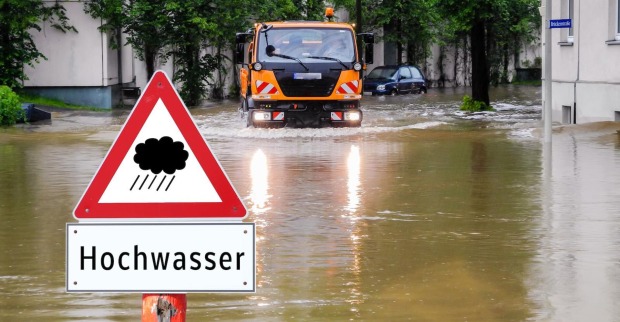 Hochwasser: Gemeinde-Lastwagen auf überschwemmter Straße und ein Hinweisschild "Hochwasser".