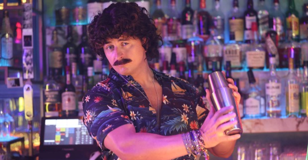 Mann mit Schnauzer steht hinter Bar und mixt Cocktails