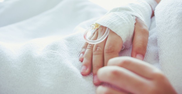 Ein kleiner Bub liegt im Spital, jemand hält seine Hand.