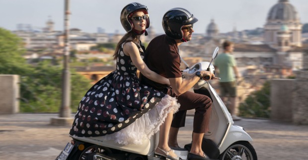 Frau fährt mit einem Mann gemeinsam auf einer Vespa durch eine Stadt