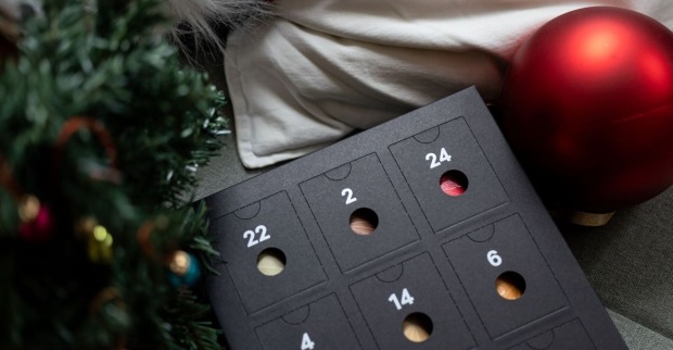 Ein Adventkalender liegt neben einer roten Christbaumkugel.