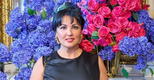 Anna Netrebko vor einer Blumenwand.