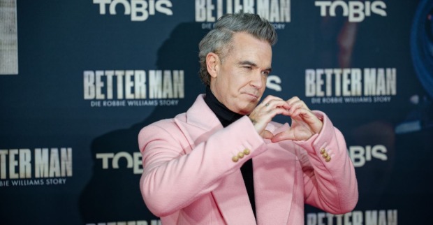 Robbie Williams formt ein Herz mit seinen Händen.