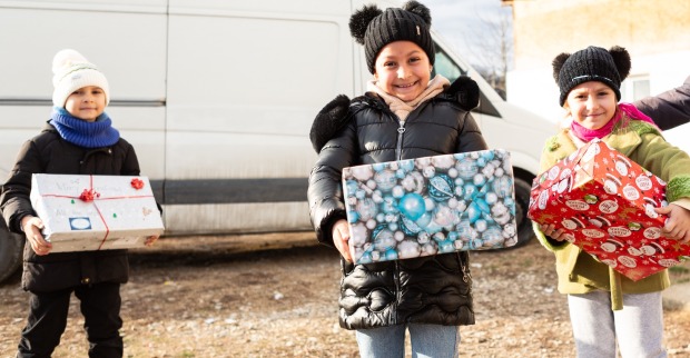 drei Kinder mit Geschenken vor einem weißen Bus