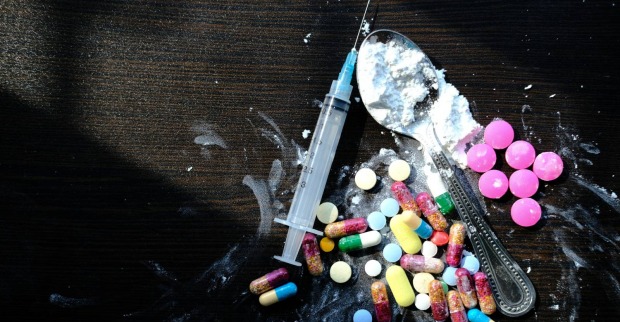Eine Auswahl unterschiedlichster Drogen und Utensilien für den Drogenkonsum auf einer schwarzen Tischplatte