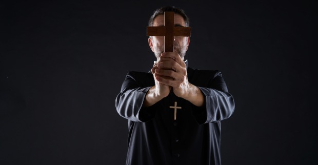 Ein Priester hält ein Kreuz vor sein Gesicht.