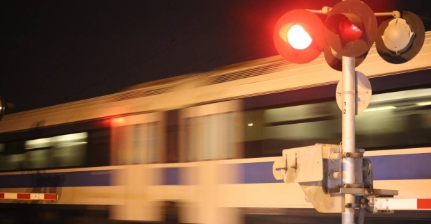 Ein verschwommen erscheinender Zug, der rasant eine Eisenbahnkreuzung überquert, während die Signalanlage rot leuchtet