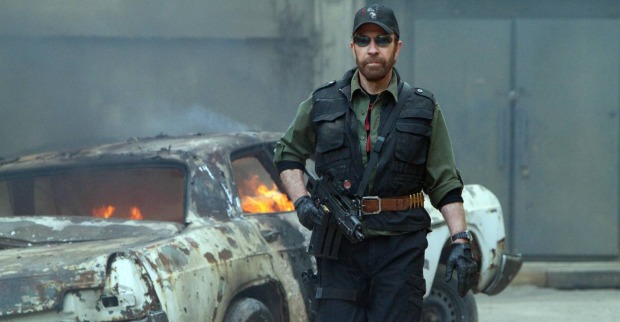 Eine Szene aus "The Expandables 2", in der Chuck Norris mit einer Maschinenpistole in der Hand neben einem brennenden Auto steht
