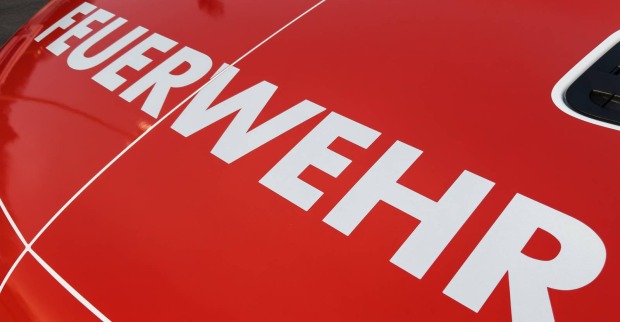Nahaufnahme der Motorhaube eines Feuerwehrfahrzeuges, auf der der weiße Schriftzug "Feuerwehr" zu lesen ist